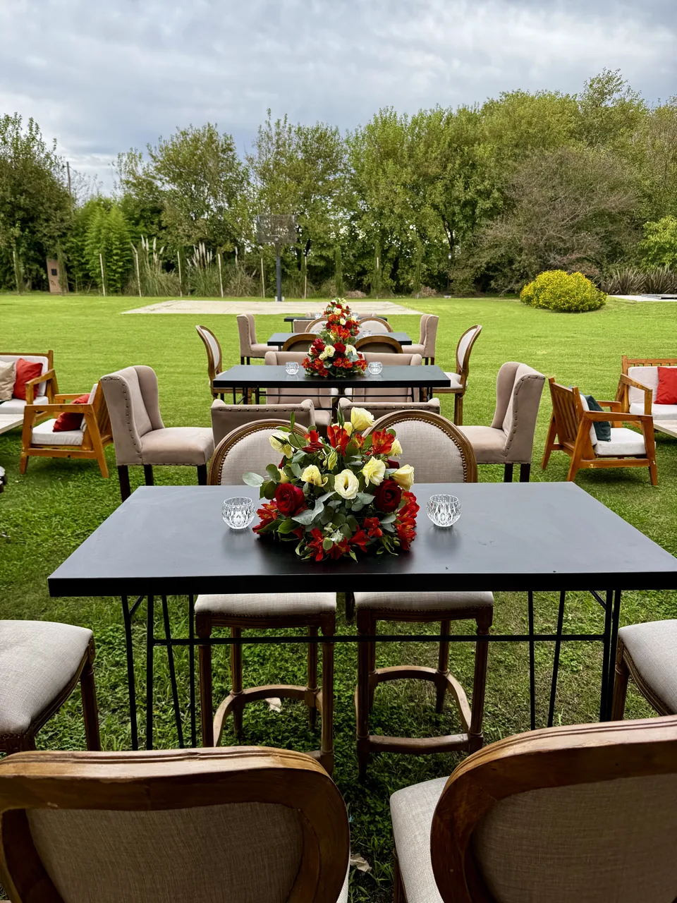 Mesas con flores y sillas frente al césped y los árboles del parque