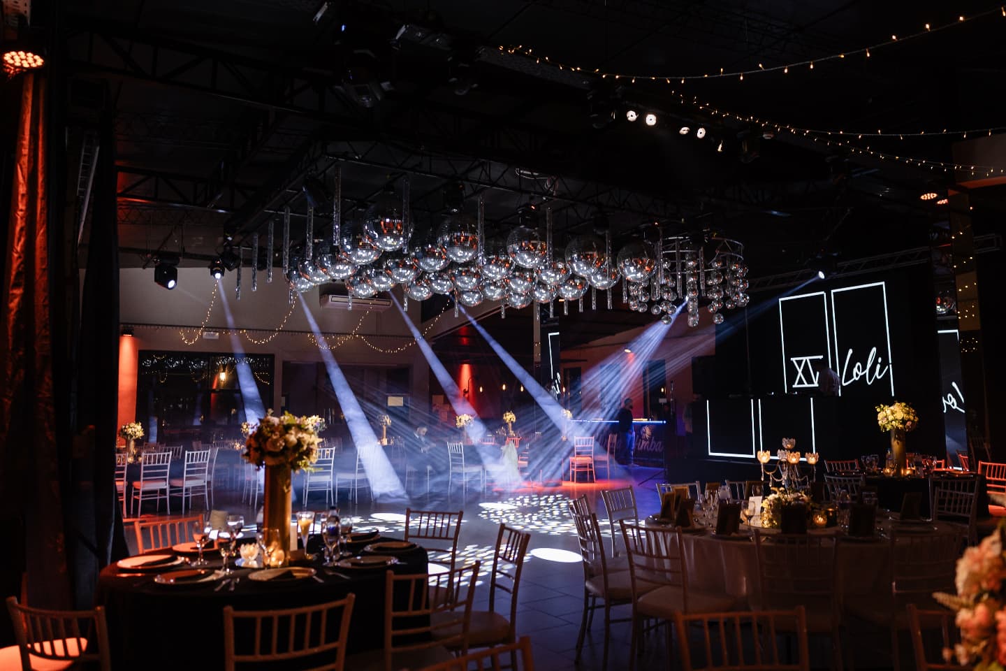 Salón preparado para una fiesta, con mesas, esferas y luces sobre la pista